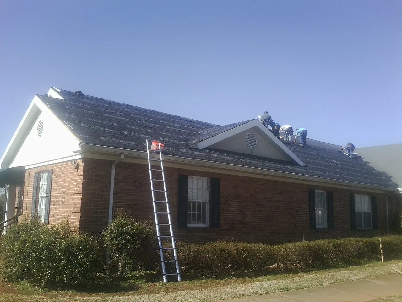Crew tearing shingles off a brick ranch roof with a ladder set — Emergency Roof Repair work by our crew in East Liverpool
