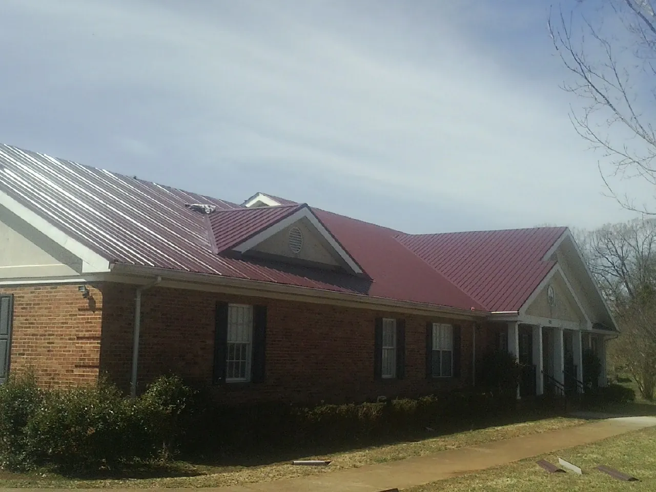 Red metal roof with gabled entries on a long brick building, from a Hail Damage Roof Repair job in East Liverpool