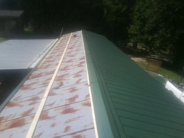 Old rusted panels beside newly installed green metal roofing in East Liverpool