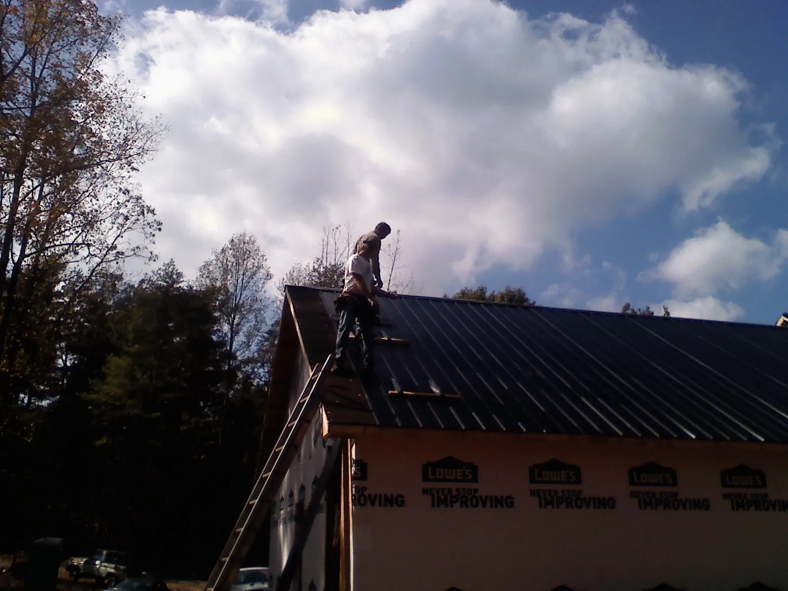 Roofer fastening dark metal panels high against a cloudy sky, from a Roof Inspection job in East Liverpool