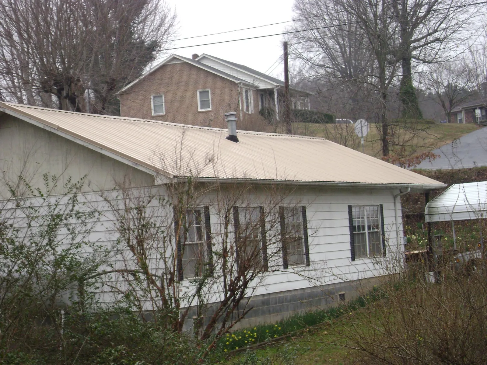 Tan metal roof on a white sided house set into a hillside — Commercial Roofing by Roofing Brothers in East Liverpool